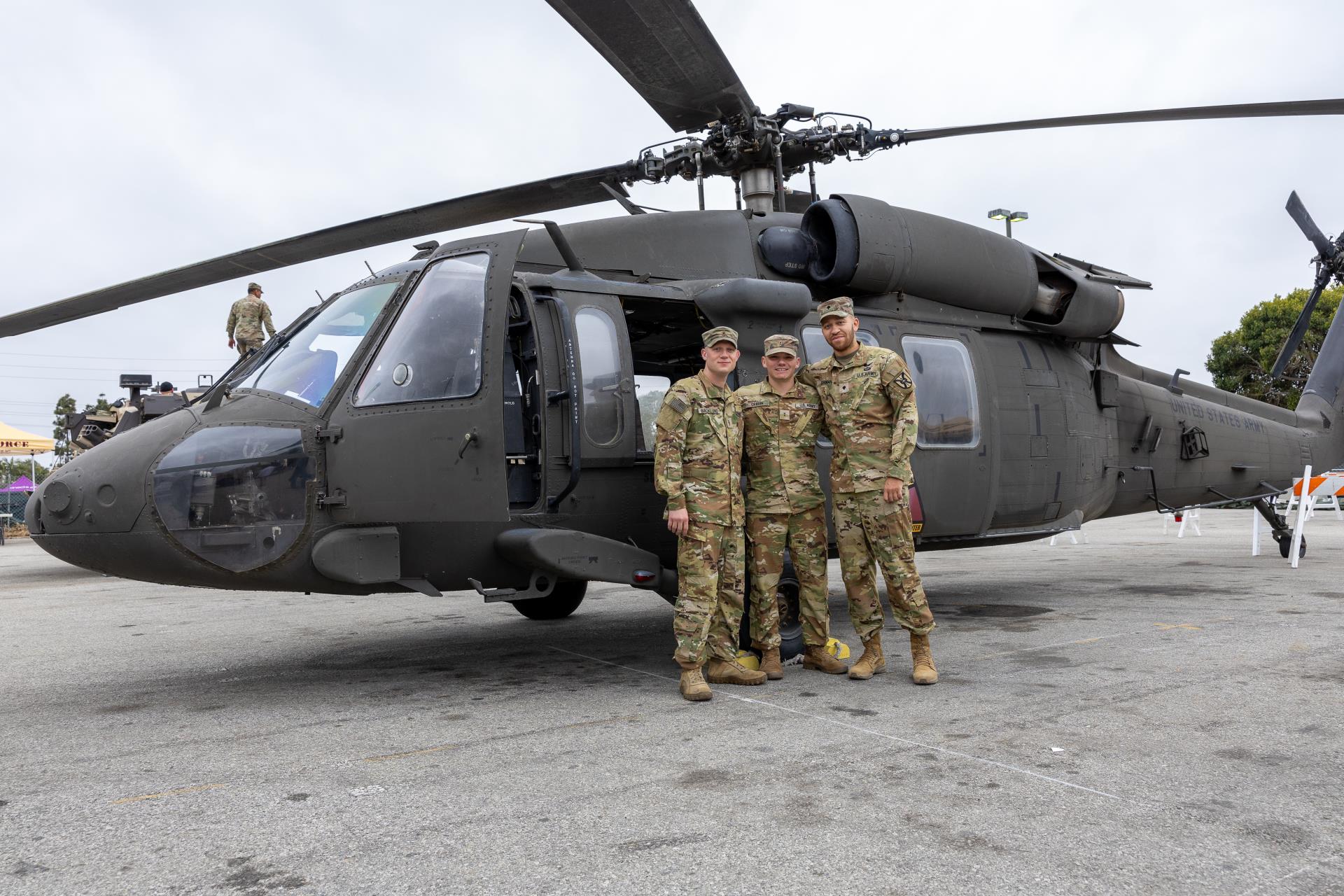 Three military personnel standing in front of a helicopter